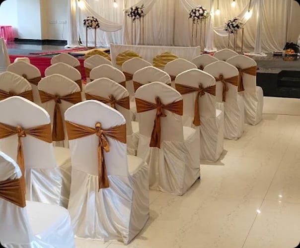 Banquet chairs in white covers with gold sashes set for a reception at Sri Sai Convention Hall, Jayanagar