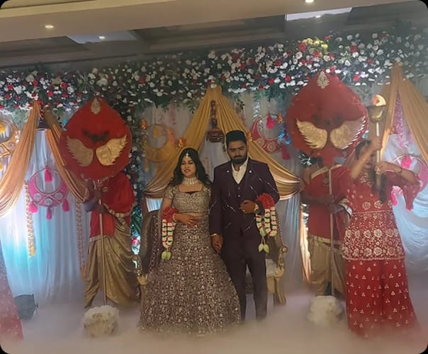 A wedding couple on the decorated stage under red and gold umbrellas at Sri Sai Convention Hall, Jayanagar